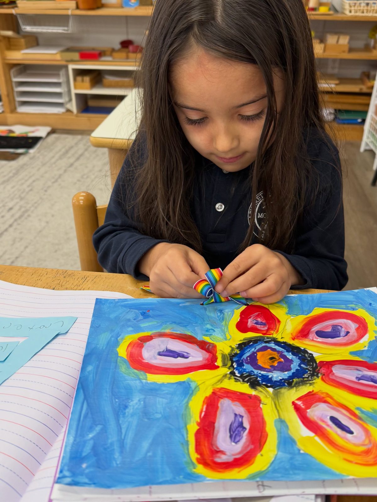 A young AIA student adding a ribbon to her bright flower painting during art in the regular school day