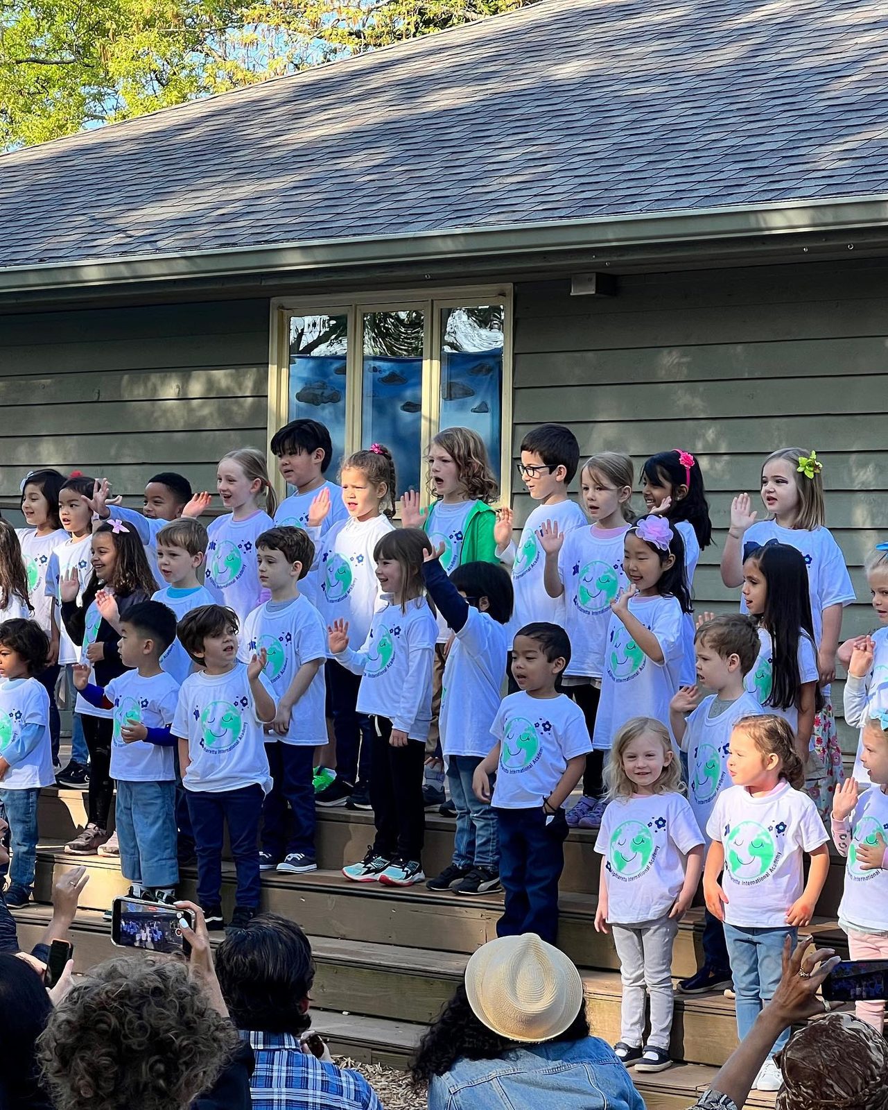 AIA students performing together as a choir on the outdoor steps while families watch