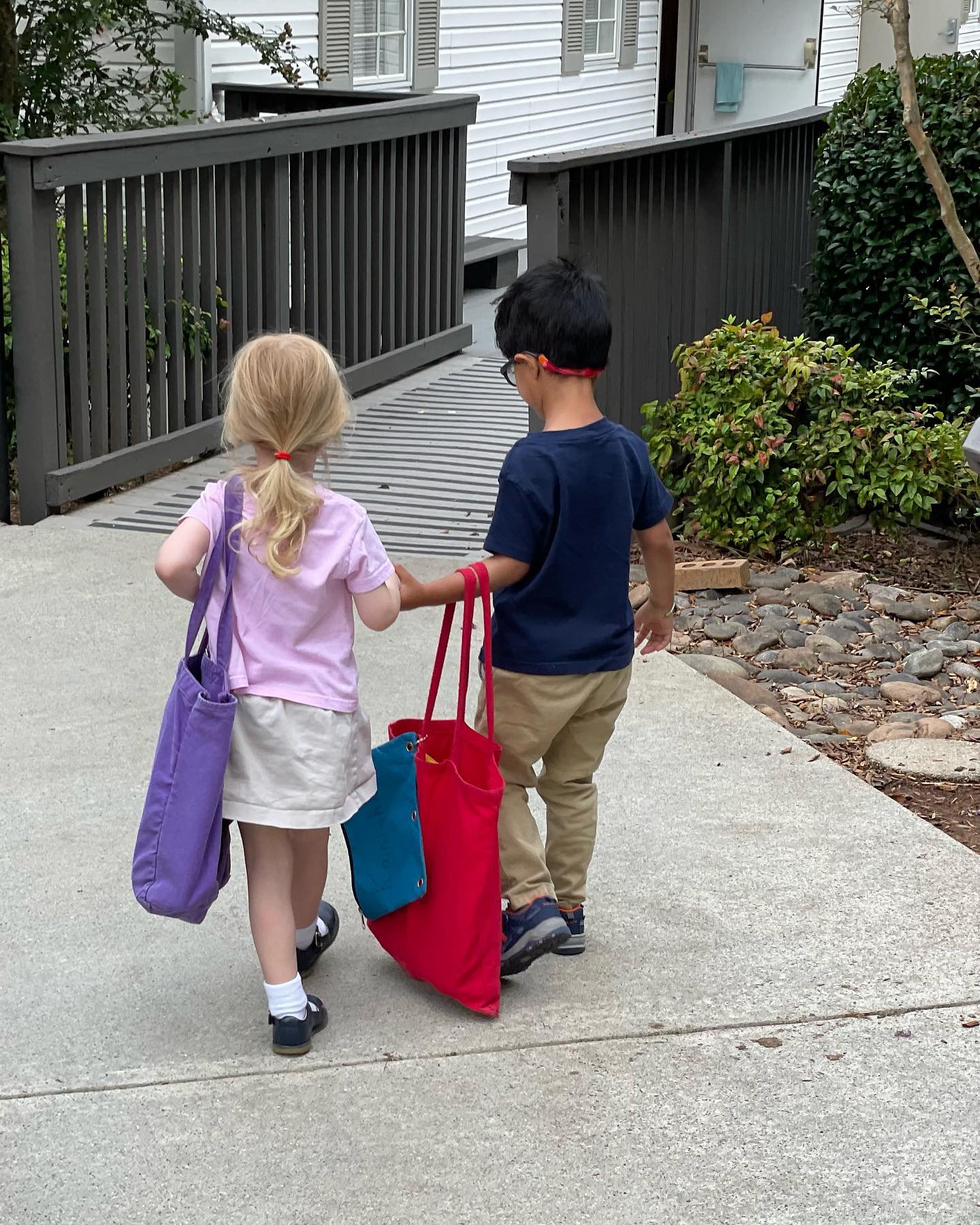 Two young AIA students walking into school together, one helping carry the other&rsquo;s tote bag
