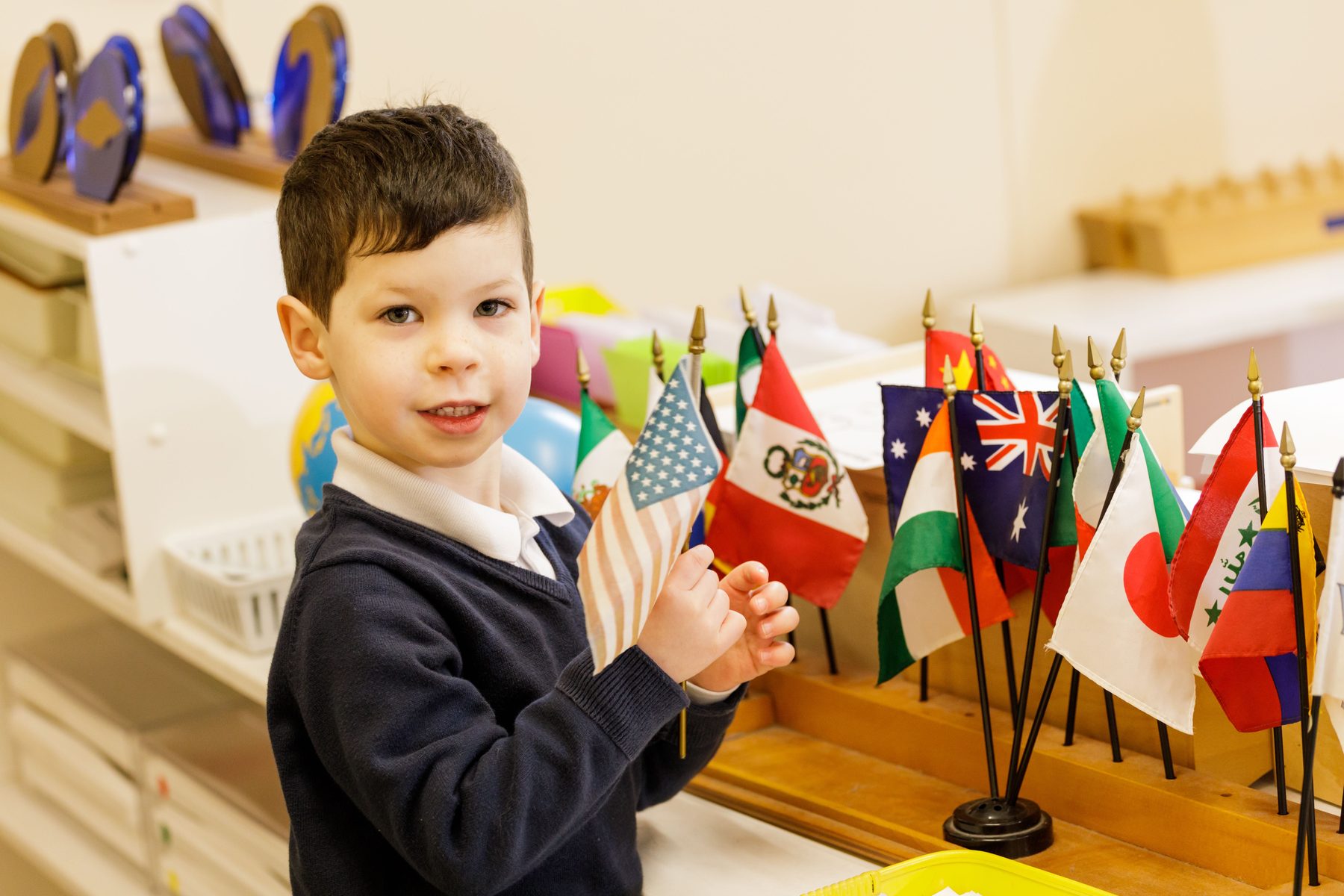 A Primary student holding a flag beside the classroom flag collection