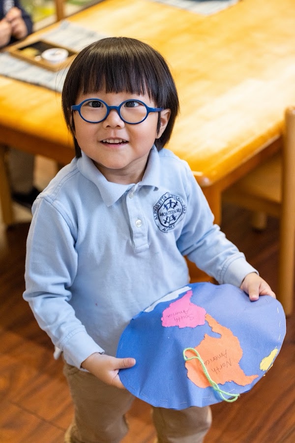 An AIA student holding a hand-assembled Montessori continent map, a hands-on geography material