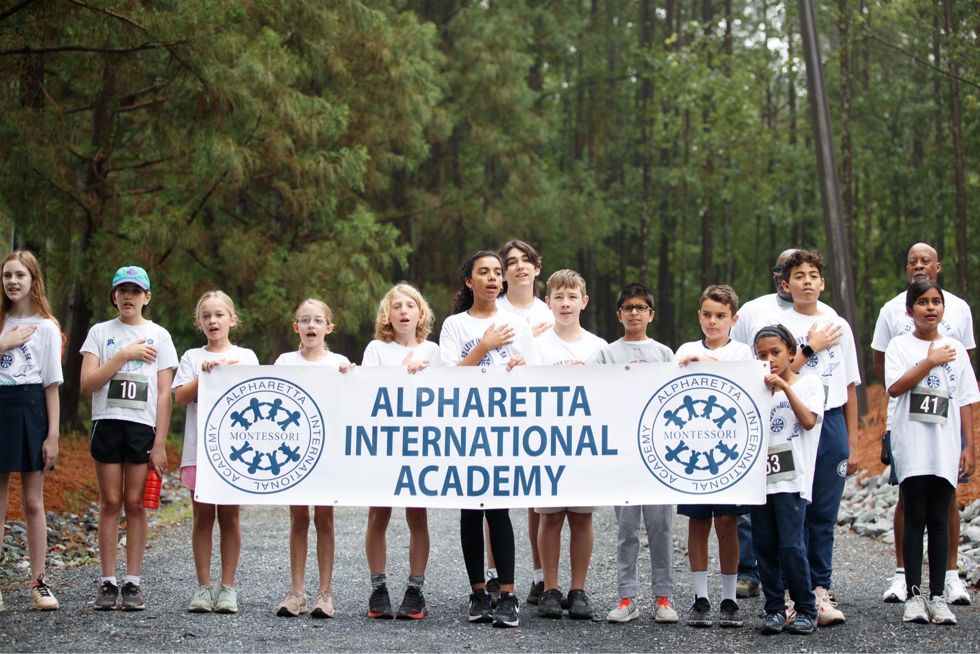 AIA students reciting the Pledge of Allegiance behind the school banner before the annual 5K race